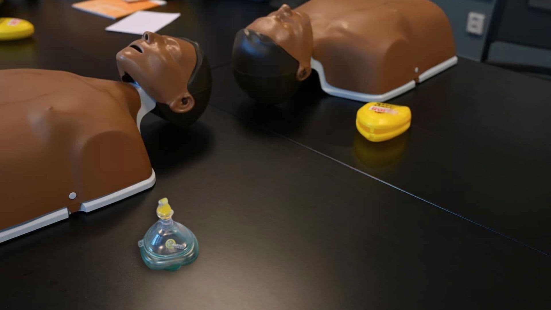 Två HLR-dockor ligger på ett svart bord, bredvid dem ligger även pocket masker.