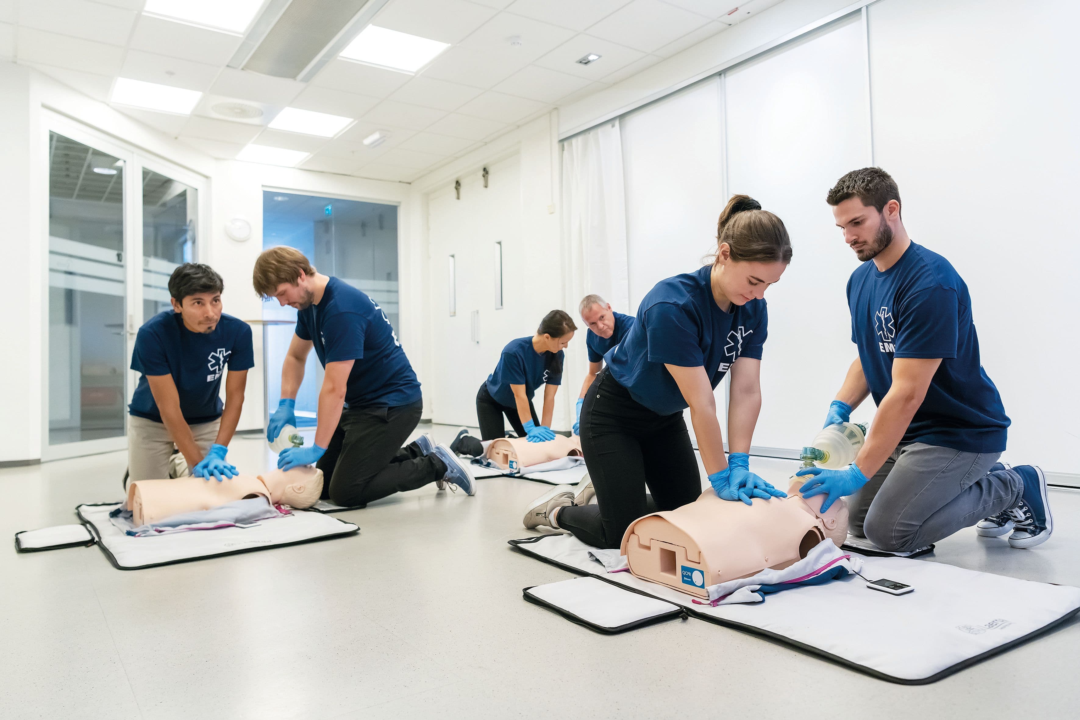 Personer sitter två och två vid HLR-dockor, de gör hjärt- och lungräddning med tvålivräddarteknik